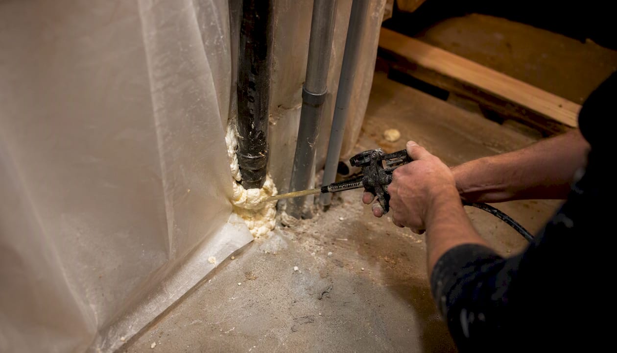 Hands sealing HVAC passage with foam in containment wall